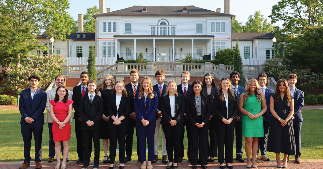 a group of students dressed in business clothing stand at the back of historic Cater Hall on auburn's campus. It is in the morning and the sun is bright and warm