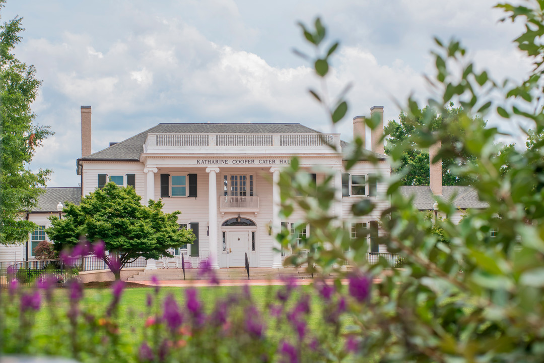image of the front of Cater Hall with purple and green plants growing in the front. 